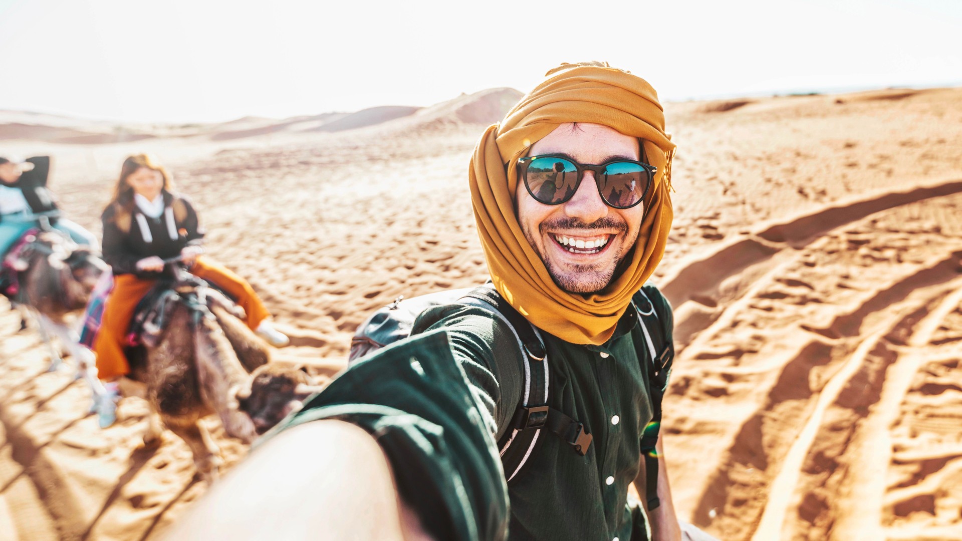 Happy tourist having fun enjoying group camel ride tour in the desert - Travel, life style, vacation activities and adventure concept